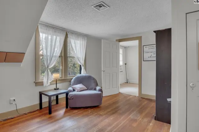This room features hardwood floors, a large window with white curtains, and a doorway to another space.