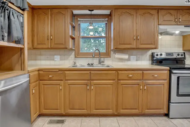 Kitchen features light wood cabinetry, a double sink, and a window above the counter.