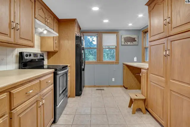 This kitchen features light wood cabinetry, a black stove, and tiled flooring.