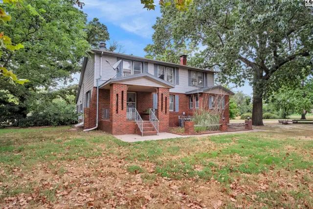 Brick and siding two-story home with a covered front porch and mature trees.