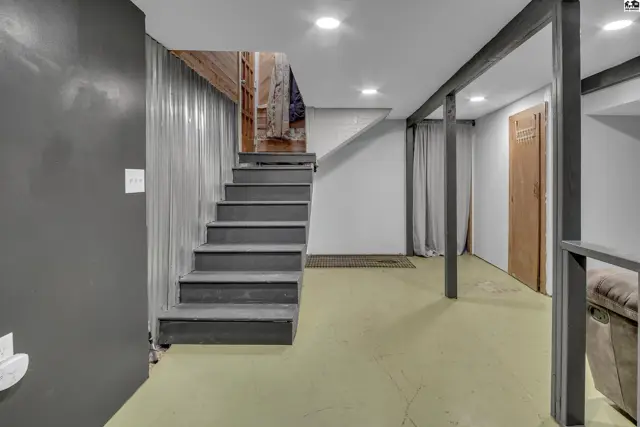 Finished basement with painted concrete floors, wood-paneled walls, and a carpeted staircase.