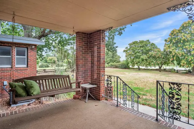 Covered porch with a swing, brick columns, and a metal railing overlooks a grassy yard.