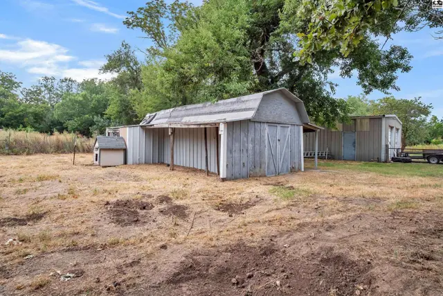Wooden barn with sliding doors and attached shed sits on dry, grassy land.
