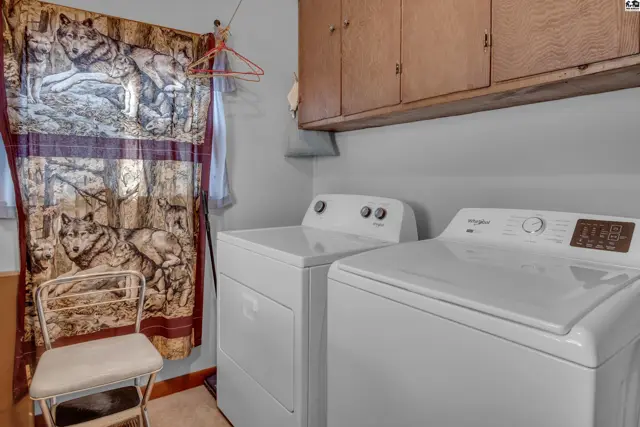 This laundry room features white washer and dryer units and a wall-mounted cabinet.