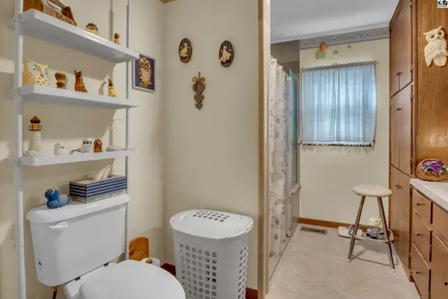 This bathroom features a toilet, shelving, and a laundry hamper next to a shower.