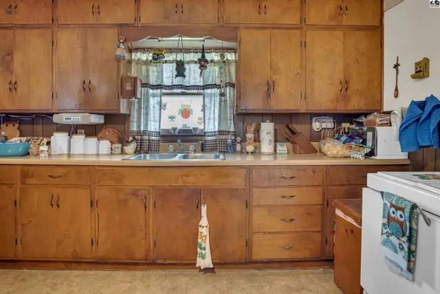 Wood cabinetry surrounds a double sink beneath a window with patterned curtains.