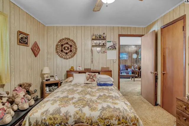Wood-paneled walls and a floral bedspread adorn this bedroom with an adjoining room.