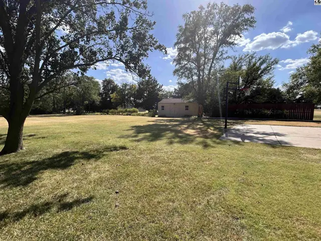 Spacious lawn surrounds a small outbuilding with a basketball hoop and paved court.