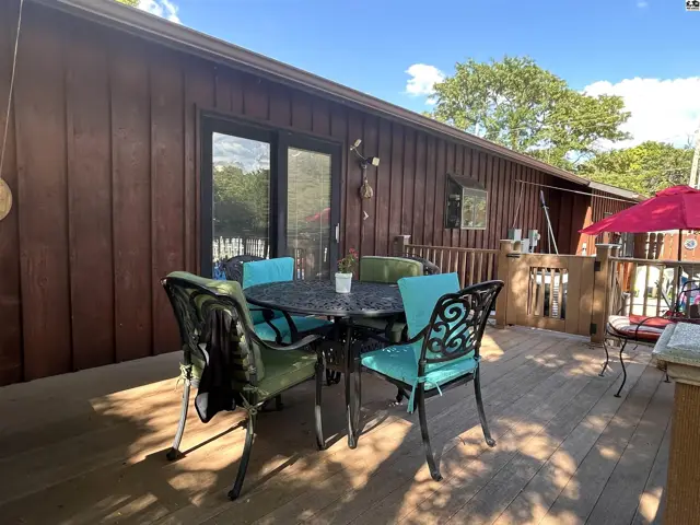 Wooden deck with a metal table and chairs, adjacent to a wood-sided building.