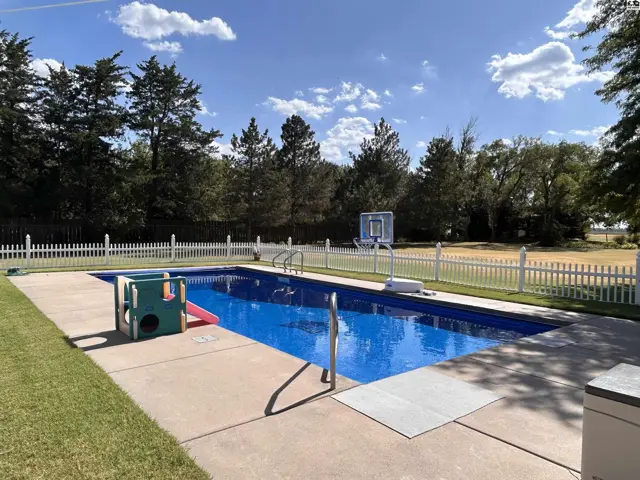 Rectangular swimming pool with concrete surround and white picket fence.