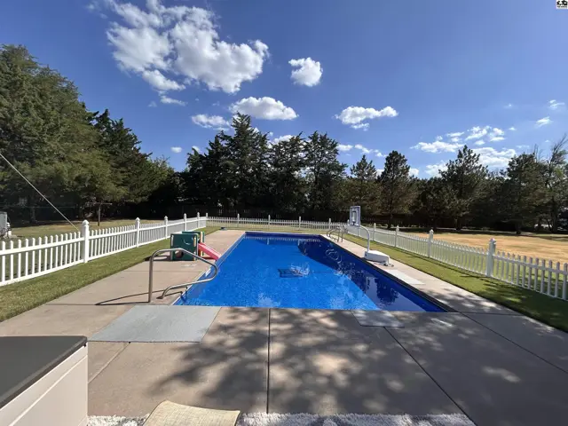 Rectangular swimming pool with concrete deck and white picket fence.