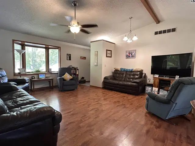 Spacious living room with hardwood floors, a bay window, and a ceiling fan.