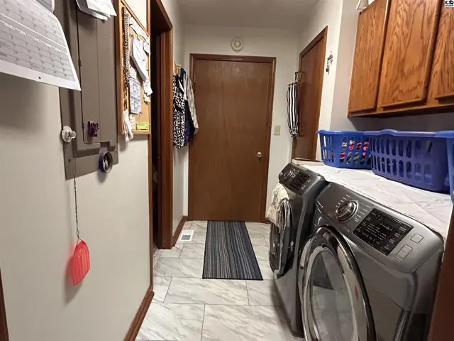 This laundry room features tile flooring, wood cabinetry, and a stacked washer and dryer.