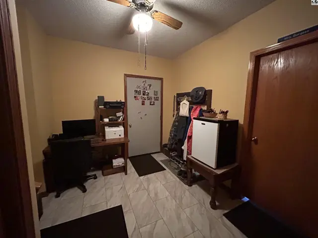 This room features a ceiling fan, tiled floor, desk, and two doors.