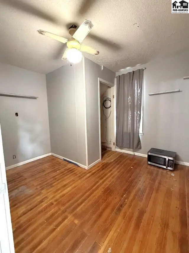This room features hardwood floors, a ceiling fan, and a closet with a curtain.