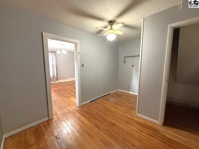This room features hardwood floors, a ceiling fan, and doorways to other spaces.