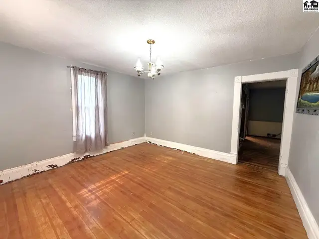 Spacious room with hardwood floors, a chandelier, and a large window.