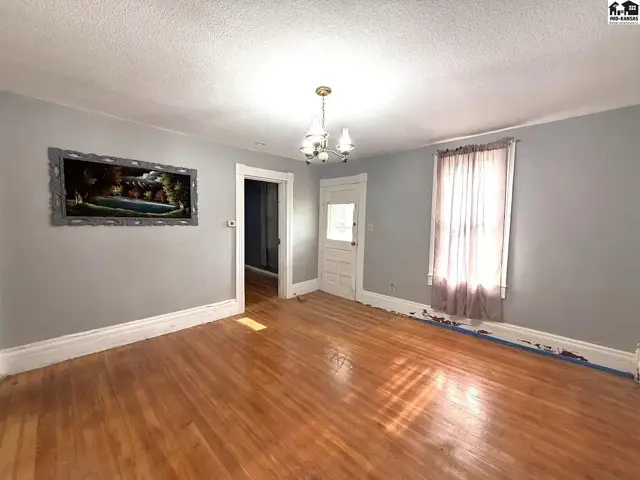 Spacious room with hardwood floors, a chandelier, and a large window.