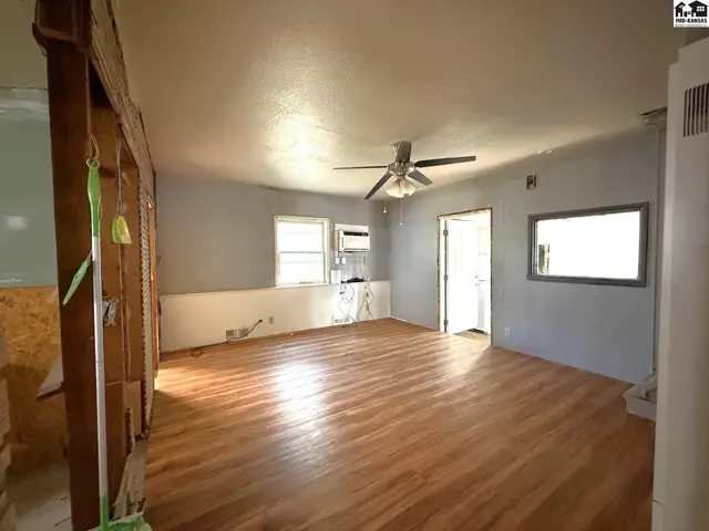 Spacious room with hardwood floors, ceiling fan, and large windows.