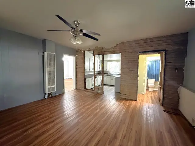 Wood floors and a ceiling fan accent this living area with views into the kitchen and bathroom.