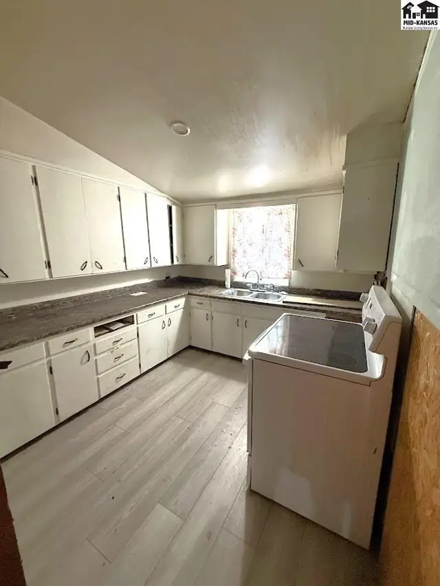 White cabinets and countertops line this kitchen with a white stove and light wood-look flooring.