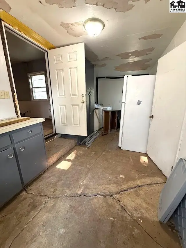 This kitchen features gray cabinets, a white refrigerator, and a cracked concrete floor.