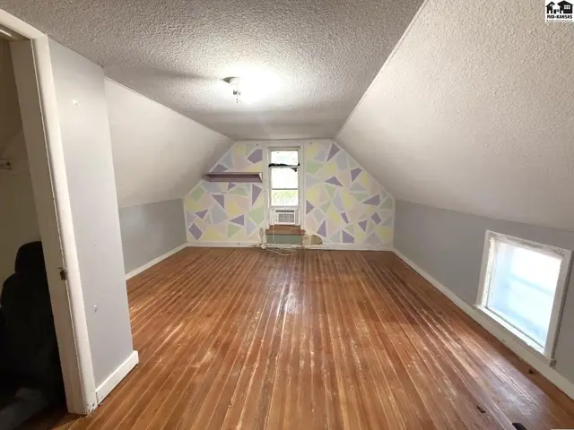 Attic room with sloped ceilings, wood floors, and a geometric patterned accent wall.