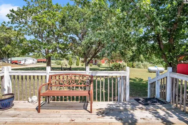 Wooden deck with white railing and metal bench overlooks a grassy yard.