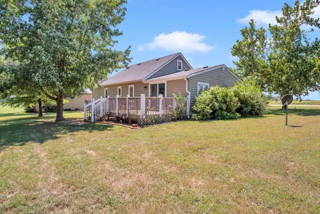 This home features a large wooden deck and mature trees on a grassy lot.