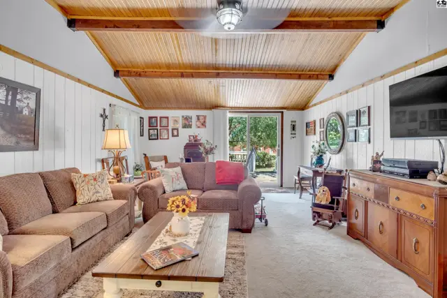 Spacious living room with wood-paneled ceiling, white paneled walls, and carpeted floors.