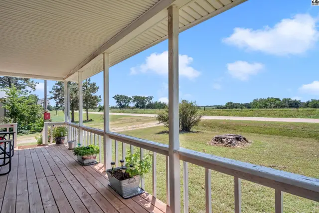 Covered porch with wooden deck and railing overlooks a rural landscape.