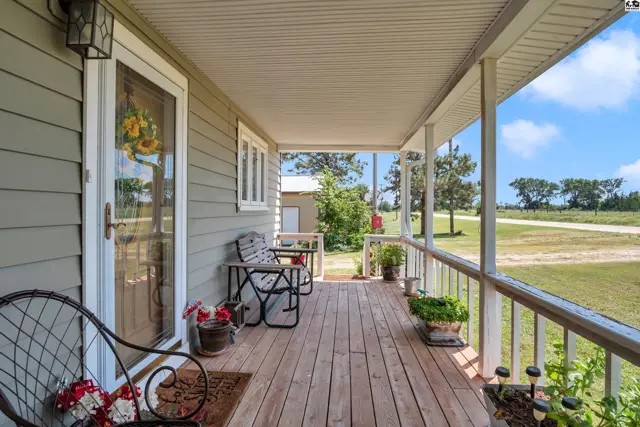 Covered wooden porch with railing, seating, and potted plants.