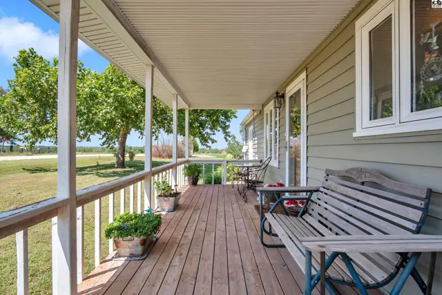 Covered wooden porch with white railings, seating, and potted plants.