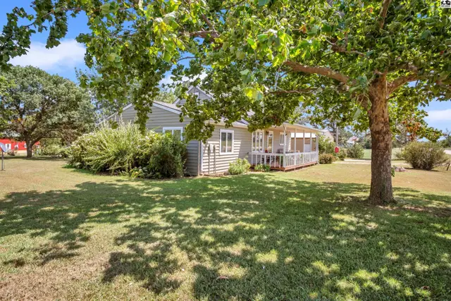 This light gray vinyl-sided home features a screened-in porch and mature trees.