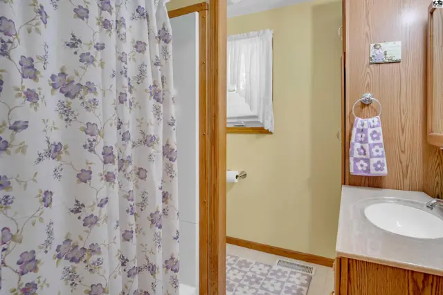 This bathroom features a shower with a floral curtain, a vanity with a sink, and light yellow walls.