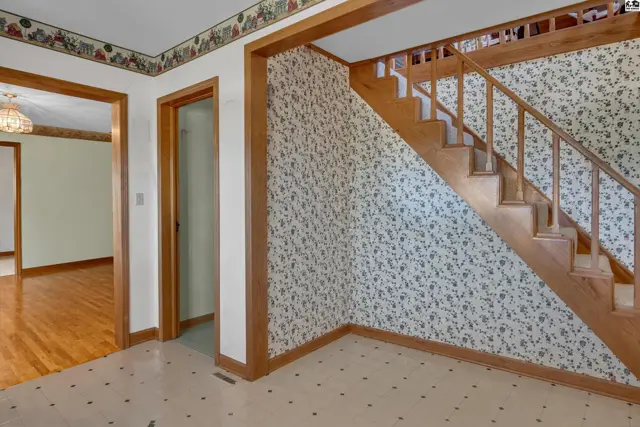 Wood-paneled staircase with patterned wallpaper and hardwood floors in the adjacent room.