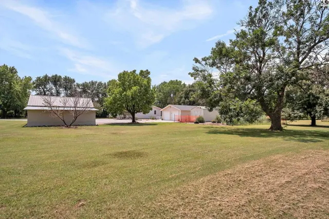 A long, low ranch-style house with a detached garage sits on a large, grassy lot.