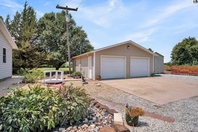 Attached two-car garage with beige siding and white doors sits on a gravel driveway.