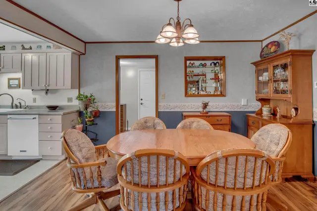 Oval wood dining table with six upholstered chairs in a room with wood cabinets and a chandelier.