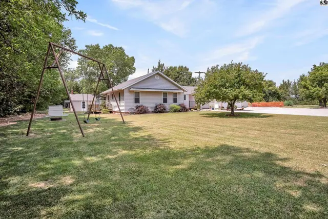 A single-story home with a detached garage sits on a grassy lot with mature trees.