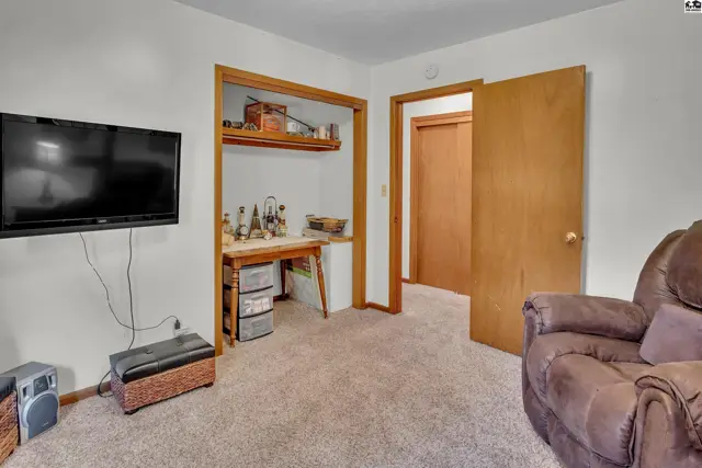 Carpeted room with a wall-mounted television and a doorway to another room.