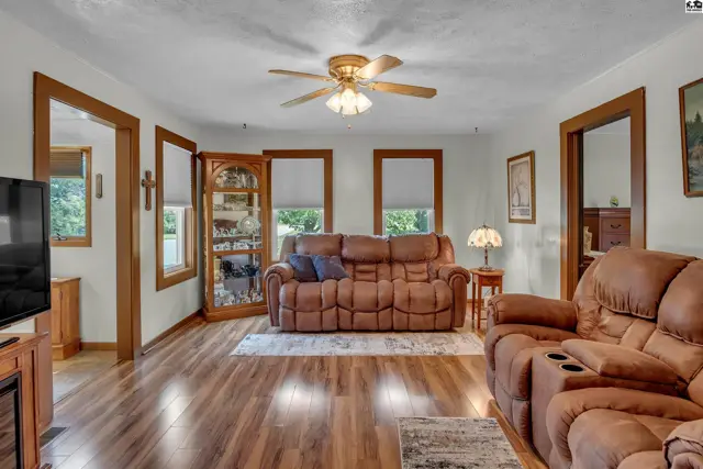 Spacious living room with hardwood floors, a ceiling fan, and large windows.