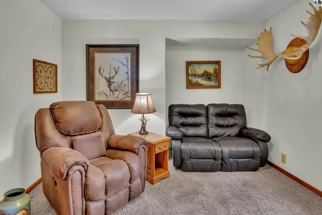 Plush recliner and loveseat sit on carpeted floor beneath mounted antlers.