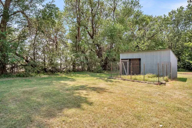 A metal shed with a double door sits on a grassy lawn surrounded by trees.