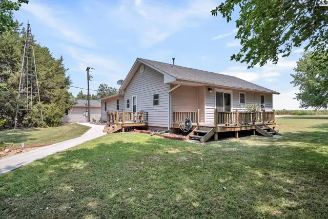 This home features a light-colored exterior with a wraparound wooden deck and mature trees.