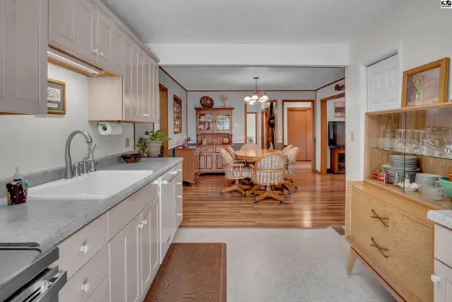 Kitchen with white cabinets and a sink opens to a dining area with a table and chairs.