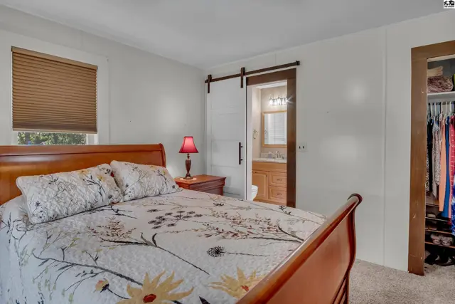This bedroom features a wooden bed frame, a sliding barn door, and a closet with clothing.