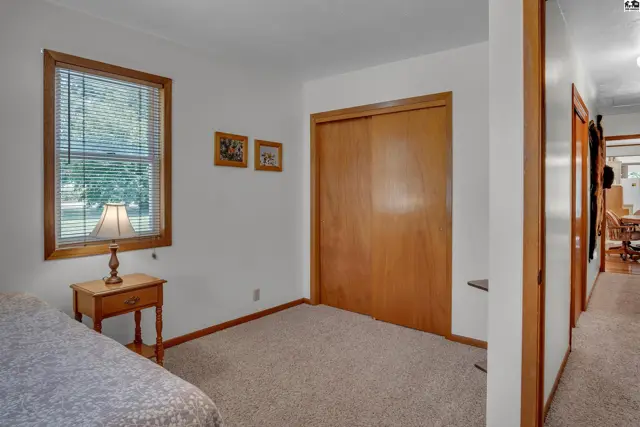 Carpeted room with a closet, window, and a wooden nightstand.