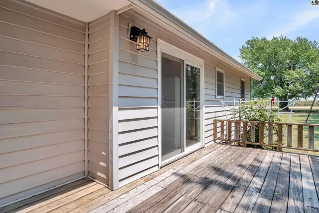 Wooden deck with a sliding glass door and exterior light fixture on a light-colored siding house.