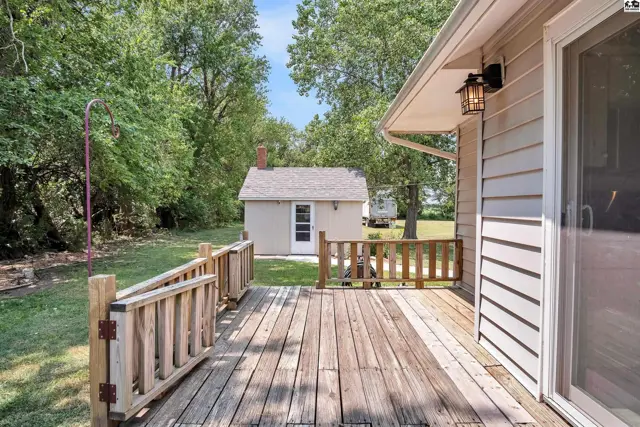 Wooden deck with railing overlooks a grassy yard with a detached shed.